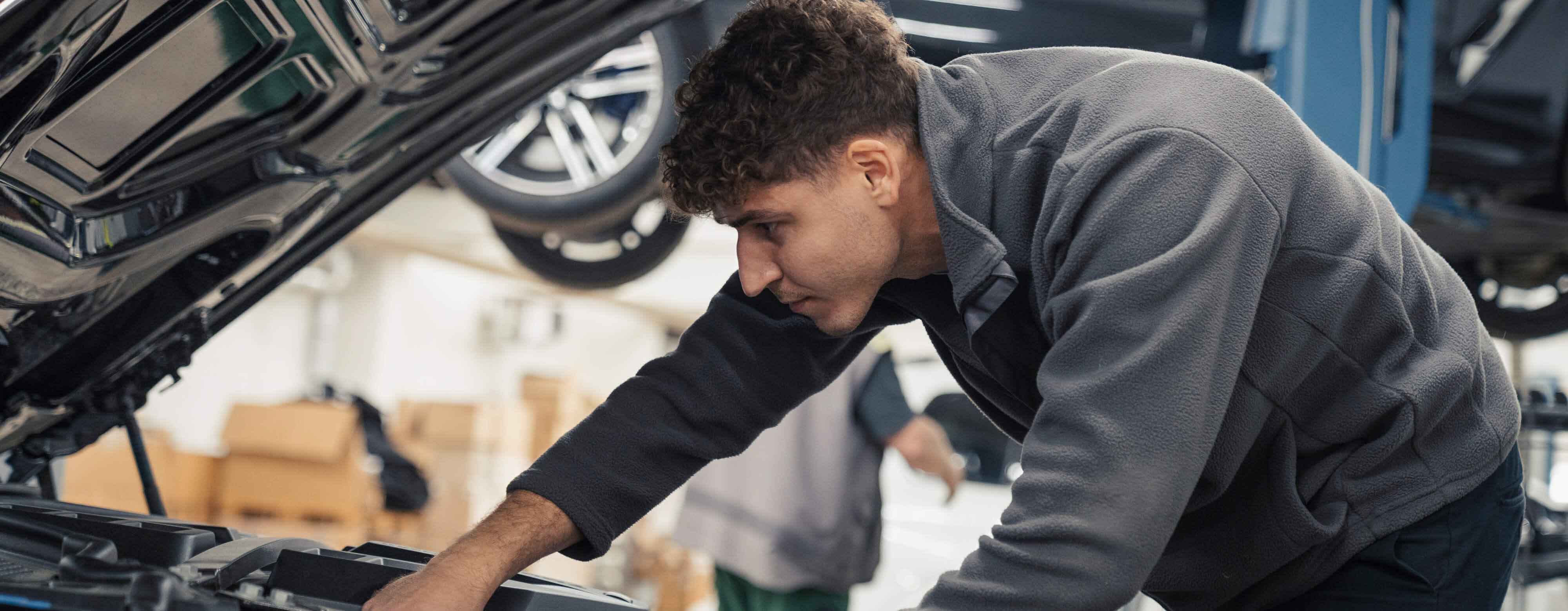Person, die über den Motorraum eines PKW gebeugt arbeitet.
