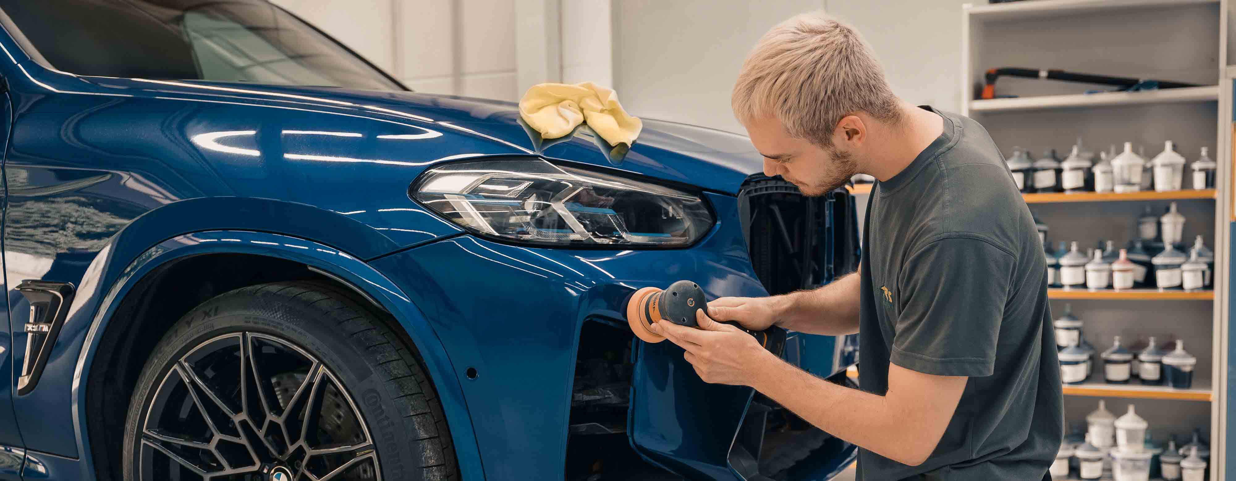 Person, die mit einem Gerät am Lack eines Autos auf einer Hebebühne arbeitet.